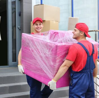 Zwei Umzugshelfer tragen ein in Folie gepacktes Möbelstück – Umzug in Calw