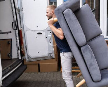 Möbellift Calw: Helfer tragen ein graues Sofa aus einem Transporter